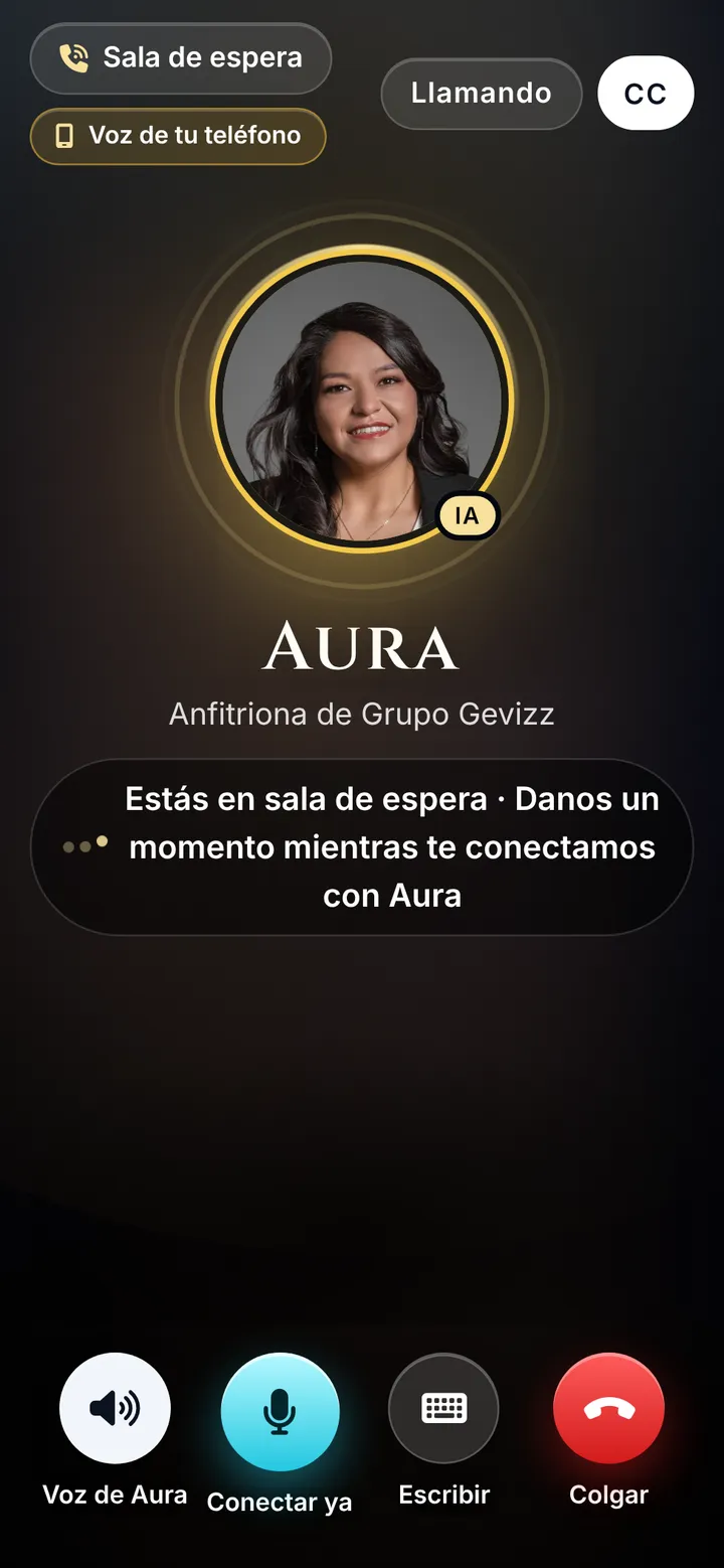 Captura de la llamada con Aura: su foto al centro con la etiqueta IA, el texto Estás en sala de espera, y abajo botones grandes Voz de Aura, Conectar ya, Escribir y Colgar; arriba, CC para subtítulos.